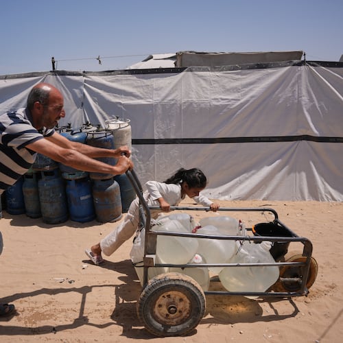 Ne'man Abu Jarad and his daughter push a cart loaded with jerrycans filled with water as they walk at a tent camp for displaced Palestinians in Khan Younis, southern Gaza Strip, Wednesday, May 13, 2026. (AP Photo/Abdel Kareem Hana)