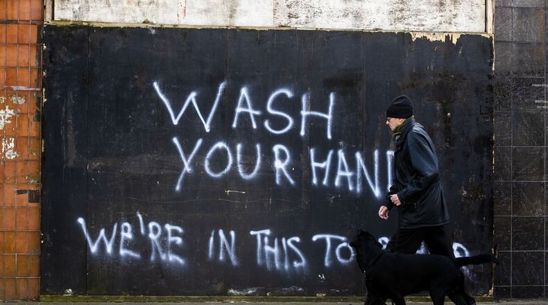A man walks a dog past graffiti with the writing, “Wash Your Hands, We’re In This Together,” on the Lower Newtownards Road in Belfast, Northern Ireland, Tuesday March 24, 2020. LIAM MCBURNEY / PA VIA AP