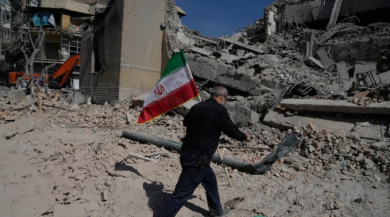 A man carries an Iranian flag to place on the rubble of a police facility struck during the U.S.–Israeli military campaign in Tehran, Iran, Wednesday, March 4, 2026. (AP Photo/Vahid Salemi)