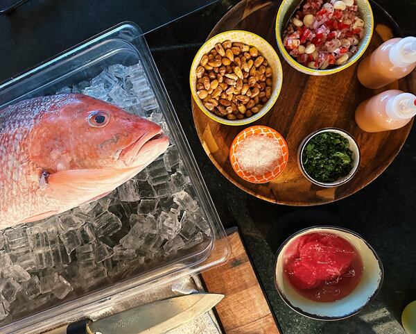 Ingredients for a homemade ceviche are laid out on a table, including a bowl of corn nuts and a full fish placed over ice.