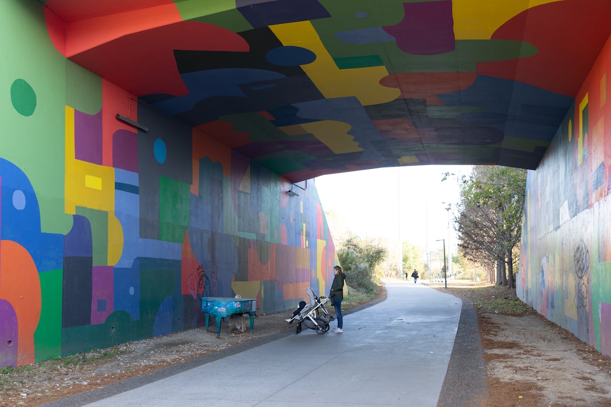 Woman walking baby in stroller and admiring piano at Beltline Northeast Trail on November 21, 2022