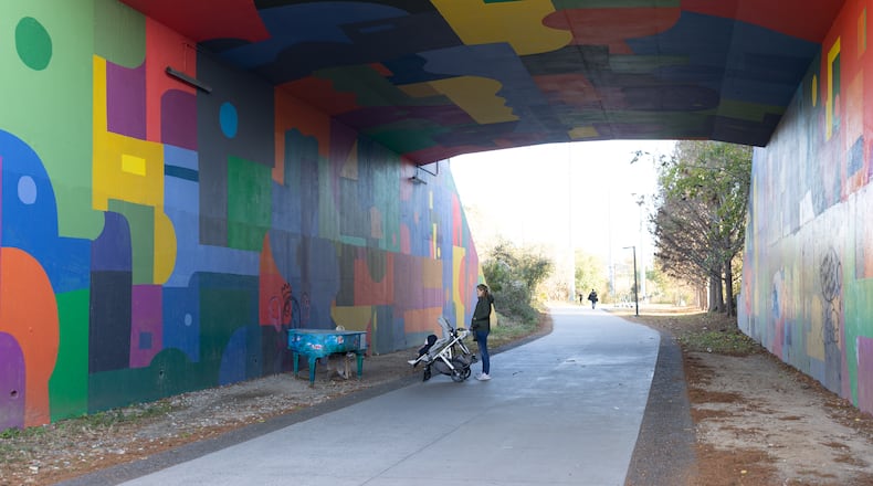 Woman walking baby in stroller and admiring piano at Beltline Northeast Trail on November 21, 2022