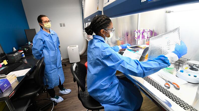 Leah Roberts opens up a delivery of COVID-19 samples for testing from a local practice as fellow Molecular Biologist Aubrey Kellison looks on, at Ipsum Diagnostics labratory on Monday, March 23, 2020. Kellison is training in order to take procedures back to West Virginia to implement. (John Amis)