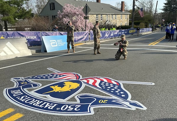 Massachusetts Army National Guard Cadet Meghan Drysdale kneels to take a photo of the road painted in commemoration of the 250th anniversary of Patriots' Day at the start of the Boston Marathon Monday, April 21, 2025. (AP Photo Jennifer McDermott)