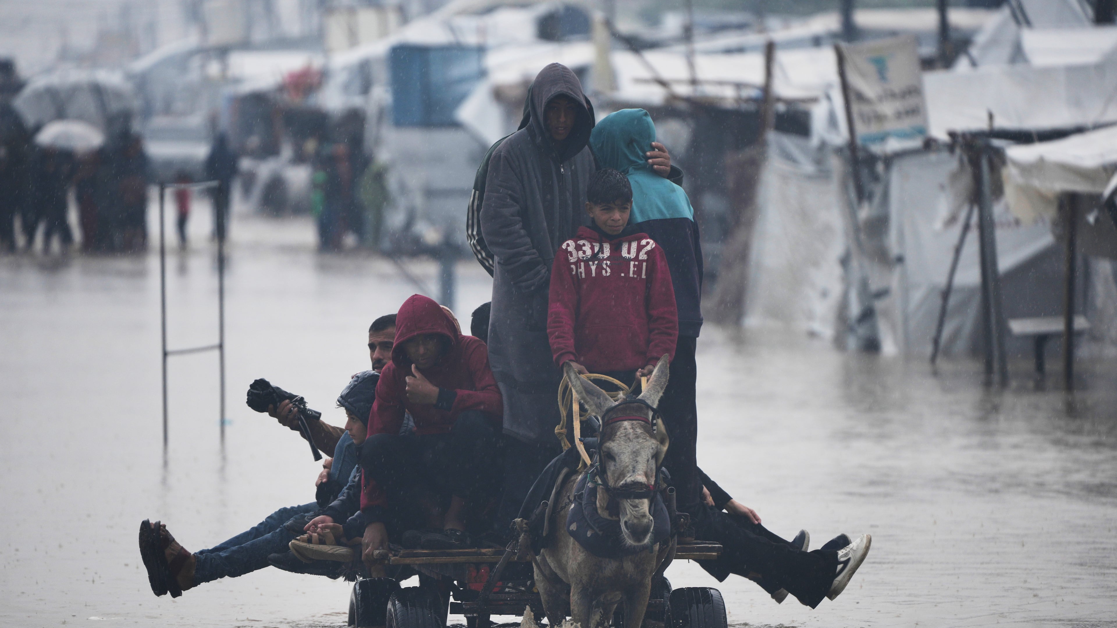 Palestinians cross a flooded street following heavy rain in Khan Younis, southern Gaza Strip, Thursday, Dec. 11, 2025. (AP Photo/Abdel Kareem Hana)