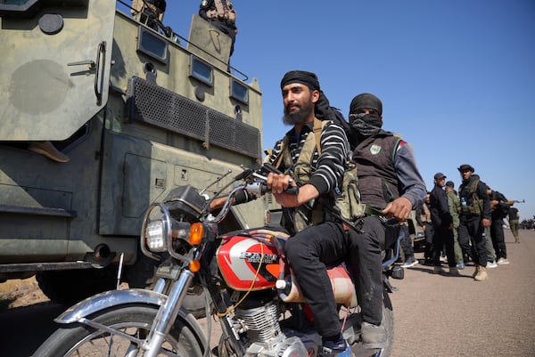 Two fighters from the Sunni Bedouin clans, ride their motorcycle as they pass by Syrian government security forces deployed on the outskirts of the Sweida province where clashes erupted between Druze militias and Sunni Bedouin clans, southern Syria, Monday, July 14, 2025. (AP Photo/Malek Khattab)