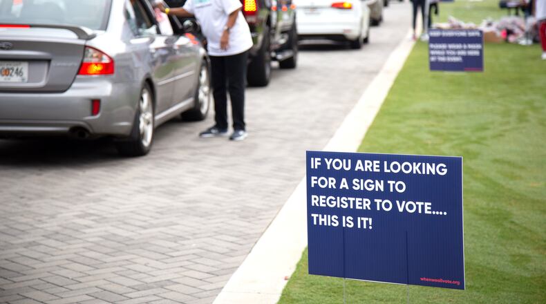Voter registrations signs line the route at a drive-thru food giveaway at The Home Depot Backyard Saturday, September 26, 2020. Event volunteers helped provide food and groceries to an estimated 2,500 attendees and prepared them to cast their ballots in November. STEVE SCHAEFER / SPECIAL TO THE AJC