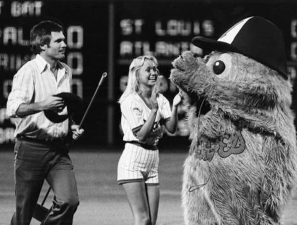 Ted Turner helps out a base sweeper during a Braves game. (AJC File)