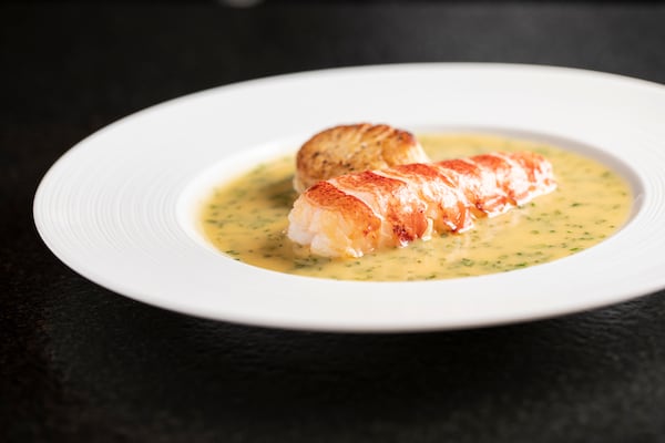 A poached lobster floats in a white bowl filled with butter.