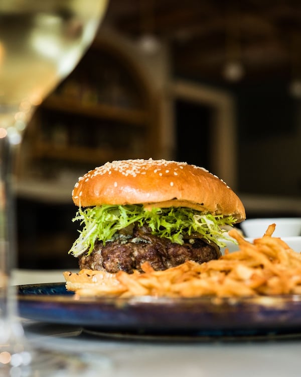 A thick cheeseburger is in focus with a pile of fries out of focus in the foreground