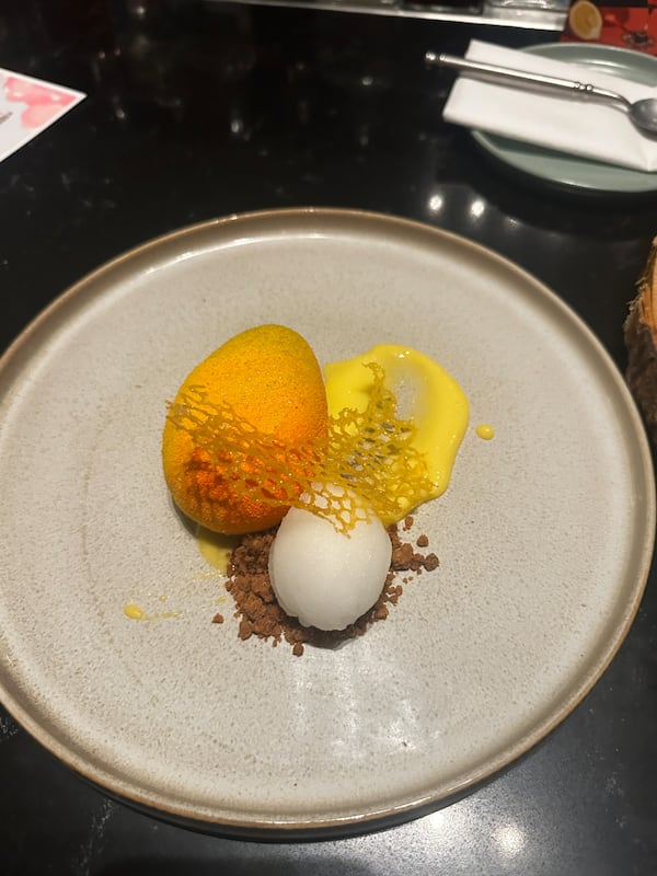 A modern dessert with a trompe l'oeil mango with a small scoop of sorbet next to it, along with a smear of bright yellow mango sauce