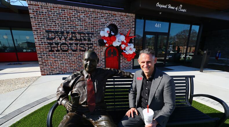 John White IV, grandson of S. Truett Cathy, sits beside a statue of his grandfather during a break from giving a tour of the newly renovated Dwarf House, the first of Truett Cathey’s restaurants. The original building was only 512 square feet, which is why Cathy called it Dwarf House, while the new renovation expands it to 10,643 square feet while preserving much of it's past.   “Curtis Compton / Curtis.Compton@ajc.com”`
