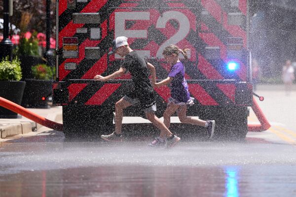 Children run through water sprayed by a fire truck to cool off outside Busch Stadium before the start of a baseball game between the St. Louis Cardinals and the Cincinnati Reds Sunday, June 22, 2025, in St. Louis. (AP Photo/Jeff Roberson)