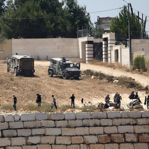 Israeli soldiers stand guard next to settlers in front of Palestinian homes that they have blockaded in the village of Qusra, south of Nablus, in the occupied West Bank, Wednesday, Aug. 12, 2026. (AP Photo/Nidal Eshtayeh)