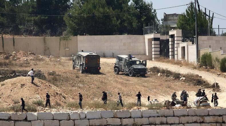 Israeli soldiers stand guard next to settlers in front of Palestinian homes that they have blockaded in the village of Qusra, south of Nablus, in the occupied West Bank, Wednesday, Aug. 12, 2026. (AP Photo/Nidal Eshtayeh)