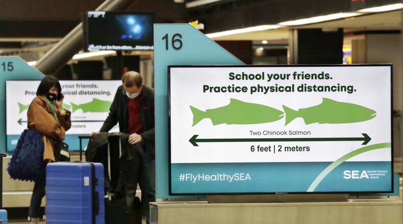 Travelers pick up luggage where signs remind them to stay six feet apart at Seattle-Tacoma International Airport Monday, May 18, 2020. (AP Photo/Elaine Thompson)