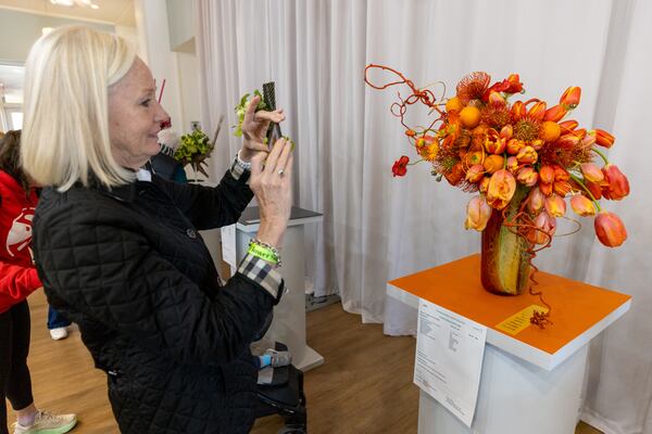 Lucy Evans takes a photograph of the  "Orange you glad spring has sprung" entry during the indoor judged competition in the division of Floral Design at the Atlanta Botanical Garden on Saturday, February 24, 2024.  (Steve Schaefer/steve.schaefer@ajc.com)