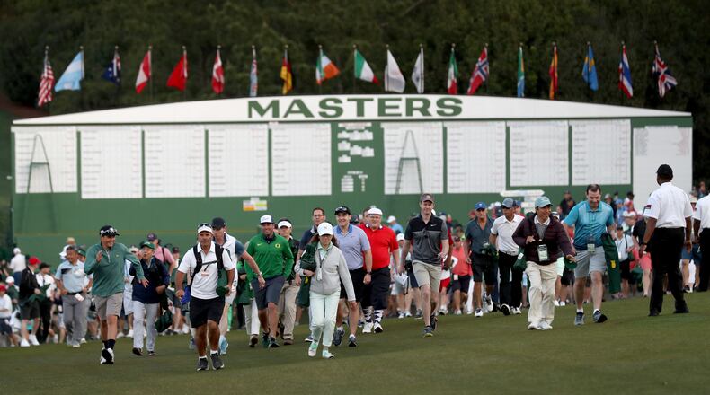 Patrons enter the grounds and walk toward the first tee crossing in front of the Masters scoreboard before the start of the 2019 tournament Thursday, April 11, 2019, at Augusta National Golf Club in Augusta.