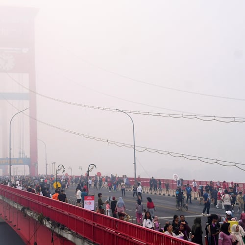People walk along the Ampera Bridge as haze from wildfires blankets the city of Palembang, in South Sumatra, Indonesia, Sunday, Aug. 23, 2026. (AP Photo/Muhammad Fajri)