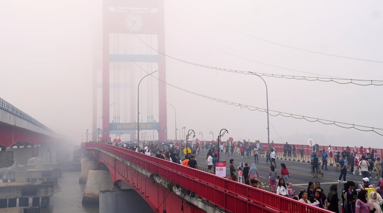 People walk along the Ampera Bridge as haze from wildfires blankets the city of Palembang, in South Sumatra, Indonesia, Sunday, Aug. 23, 2026. (AP Photo/Muhammad Fajri)