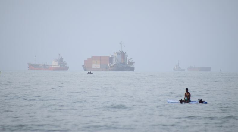 FILE - A man sits on a surfboard as a container ship and other commercial vessels appear anchored in the Strait of Hormuz off Bandar Abbas, Iran, Monday, July 27, 2026. (Razieh Poudat/ISNA via AP, File)