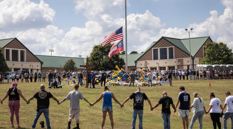 Mourners hold arms in a ring around a makeshift memorial at Apalachee High School in Winder, Ga., on Saturday, Sept. 7, 2024. As residents in Winder, Ga., consoled one another, questions rose about whether more could have been done to prevent the attack in which a gunman killed two students and two teachers last week at Apalachee High School. (Christian Monterrosa/The New York Times)