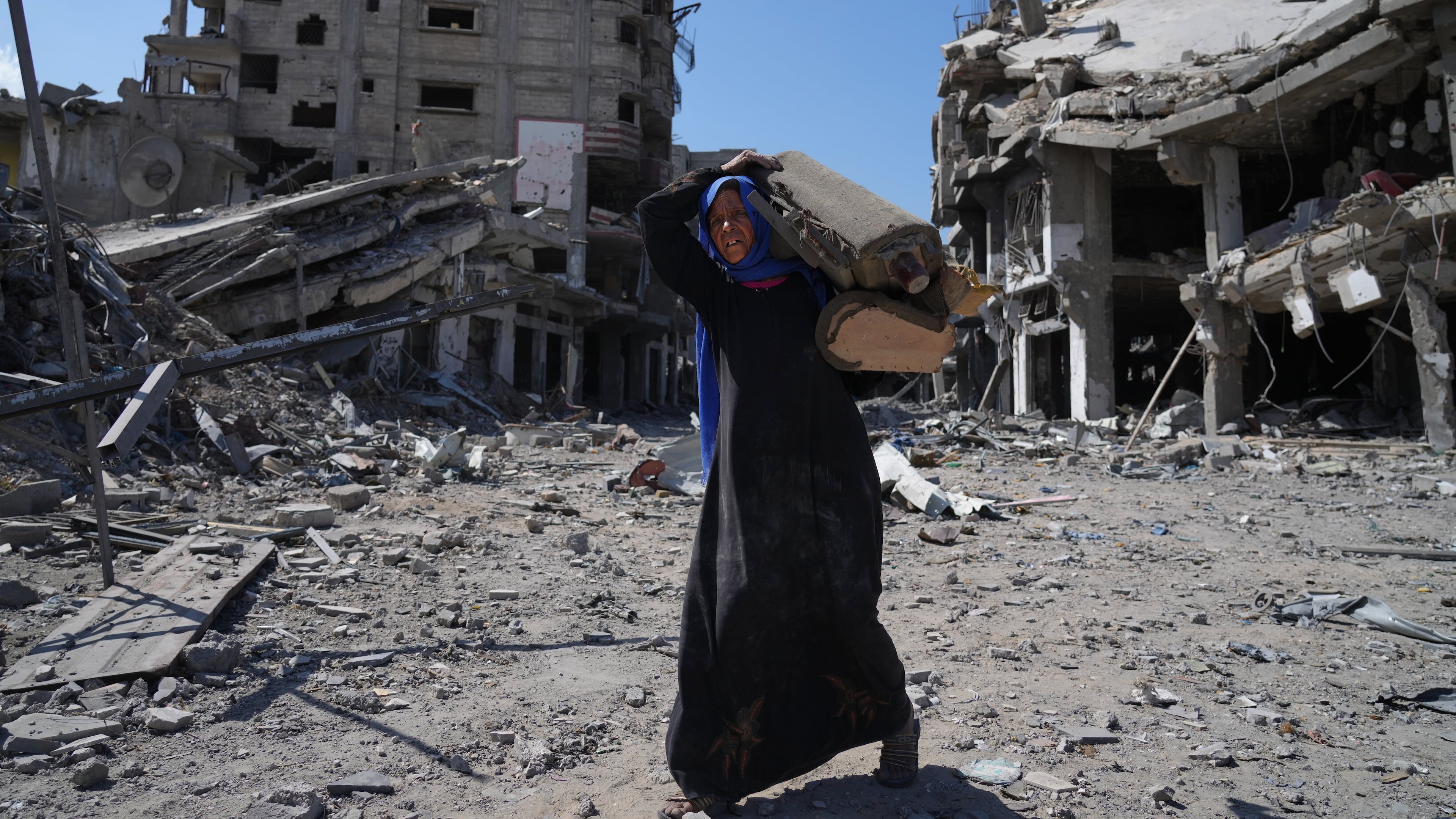 An elderly displaced Palestinian woman carries an item past destroyed buildings in Khan Younis, southern Gaza Strip, Friday, Oct. 10, 2025, after Israel and Hamas agreed to a pause in their war and the release of the remaining hostages. (AP Photo/Jehad Alshrafi)