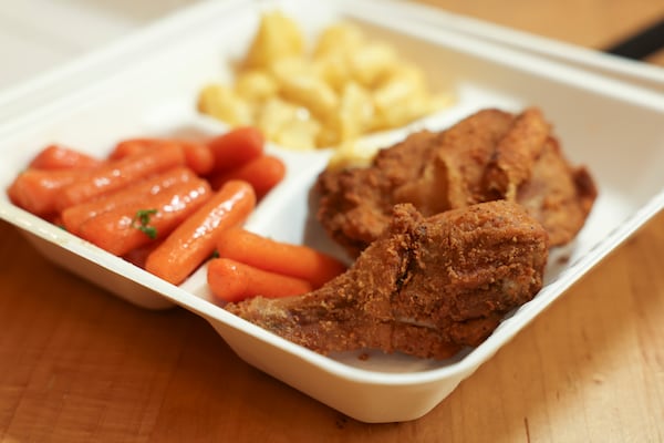 A takeout container with fried chicken, corn and macaroni and cheese.