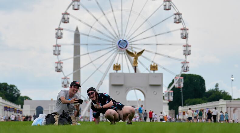 Christine Bayly, right, and Jason Brown, left, take a photo as they eat lunch on the National Mall with the Washington Monument, Freedom 250 Ferris Wheel, and a replica of the triumphal arch, behind them during the Great American State Fair, Friday, June 26, 2026, in Washington. (AP Photo/Carolyn Kaster)
