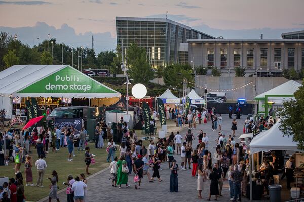 A crowd of people mills around at the Atlanta Food & Wine Festival with tents and lights.