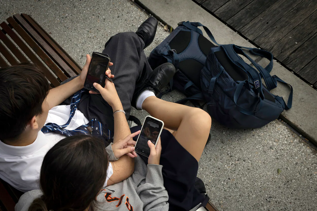 School children use their smartphones near the Barangaroo Ferry Terminal in Sydney, Feb. 24, 2021. (Matthew Abbot/The New York Times)