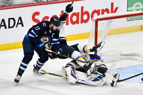 St. Louis Blues' Jake Neighbours, center, falls over Blues goaltender Jordan Binnington, right, as he is checked by Winnipeg Jets' Adam Lowry (17) during the third period of Game 2 of a first-round NHL hockey playoff series in Winnipeg, Manitoba, Monday April 21, 2025. (Fred Greenslade/The Canadian Press via AP)