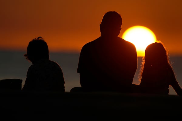 FILE - Beach goers sit on the sand as they watch the sun rise over the Atlantic Ocean, Tuesday, Feb. 28, 2023, in Surfside, Fla. (AP Photo/Wilfredo Lee, File)