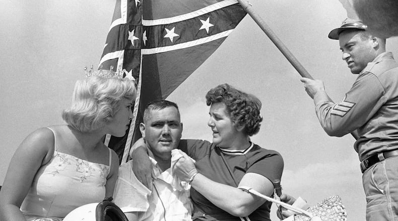 In this Sept. 3, 1962, file photo, a confederate flag waves behind Junior Johnson as he poses with his sister, right, and Miss Sun Fun U.S.A. in the winner's circle after the Southern 500 auto race at Darlington Speedway. (AP Photo/Perry Aycock, File)