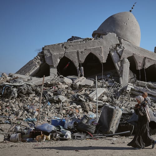 A Palestinian woman carrying her child walks past a destroyed mosque in Gaza City Sunday, Oct. 26, 2025. (AP Photo/Jehad Alshrafi)