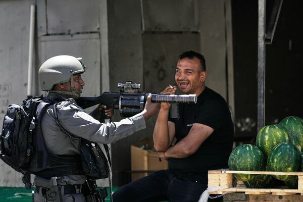 An Israeli border police officer takes up position next to a watermelon vendor, during a military raid in the Askar refugee camp near the West Bank city of Nablus, Tuesday, May 20, 2025. (AP Photo/Majdi Muhammad)