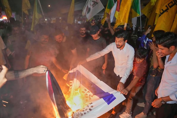 Protesters burning depictions of the Israeli and U.S. flags during a protest against Israeli attacks on multiple cities across Iran at a bridge leading to the fortified Green Zone where the U.S. Embassy is located in Baghdad, Iraq, Thursday, June 19, 2025. (AP Photo/Hadi Mizban)