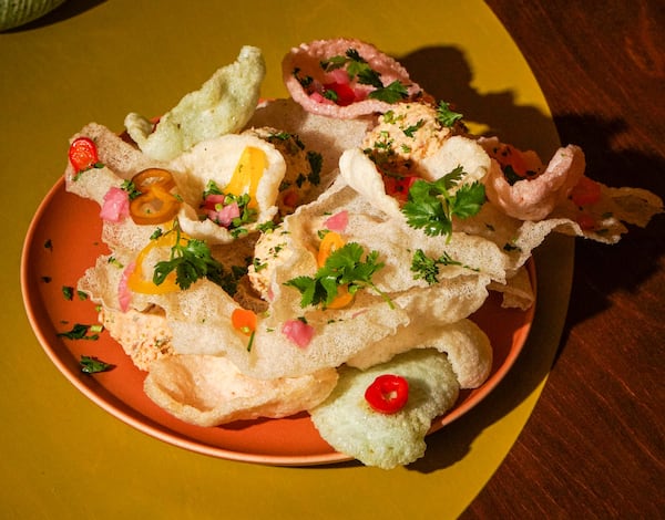 A plate overflowing with rice crackers sitting on top of scoops of fish dip, garnished with slices of small red and yellow peppers as well as cilantro