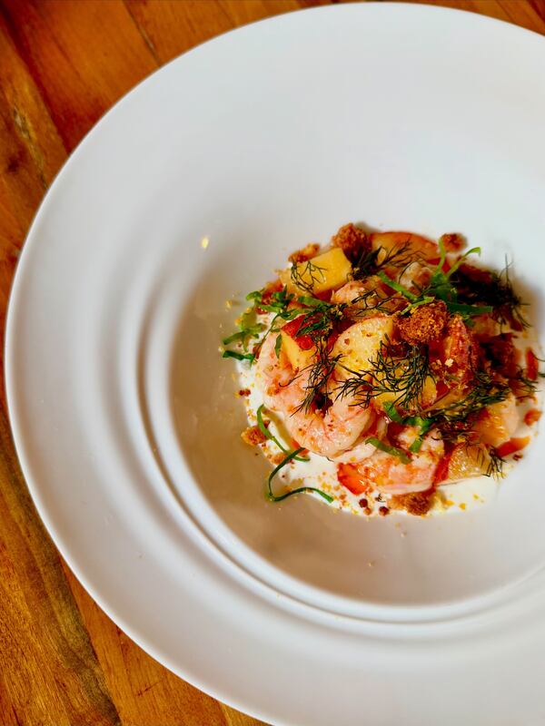 A plate containing a peach and shrimp salad, garnished with fresh herbs. The plate is on a wooden tabletop.