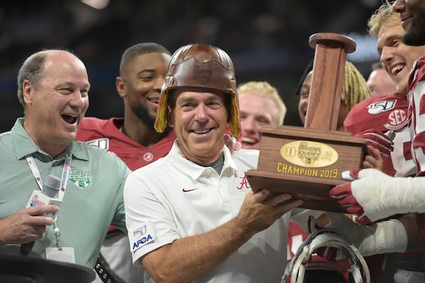 Peach Bowl Inc. CEO Gary Stokan (left) watches Alabama then-coach Nick Saban try on the "old leather helmet" from the Chick-fil-A Kickoff trophy at Mercedes-Benz Stadium in 2019.  (Courtesy Vasha Hunt via Abell Images for Chick-fil-A Kickoff)