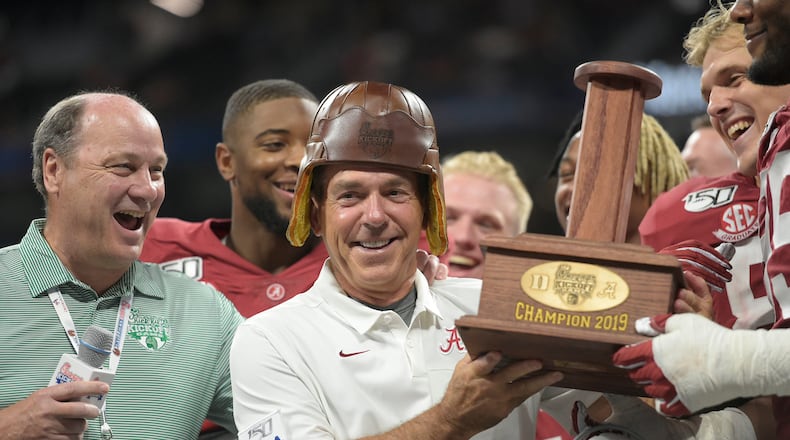 Peach Bowl Inc. CEO Gary Stokan (left) watches Alabama coach Nick Saban try on the "Old Leather Helmet" from the Chick-fil-A Kickoff trophy at Mercedes-Benz Stadium on Aug. 31, 2019. (Vasha Hunt via Abell Images, courtesy of Chick-fil-A Kickoff)