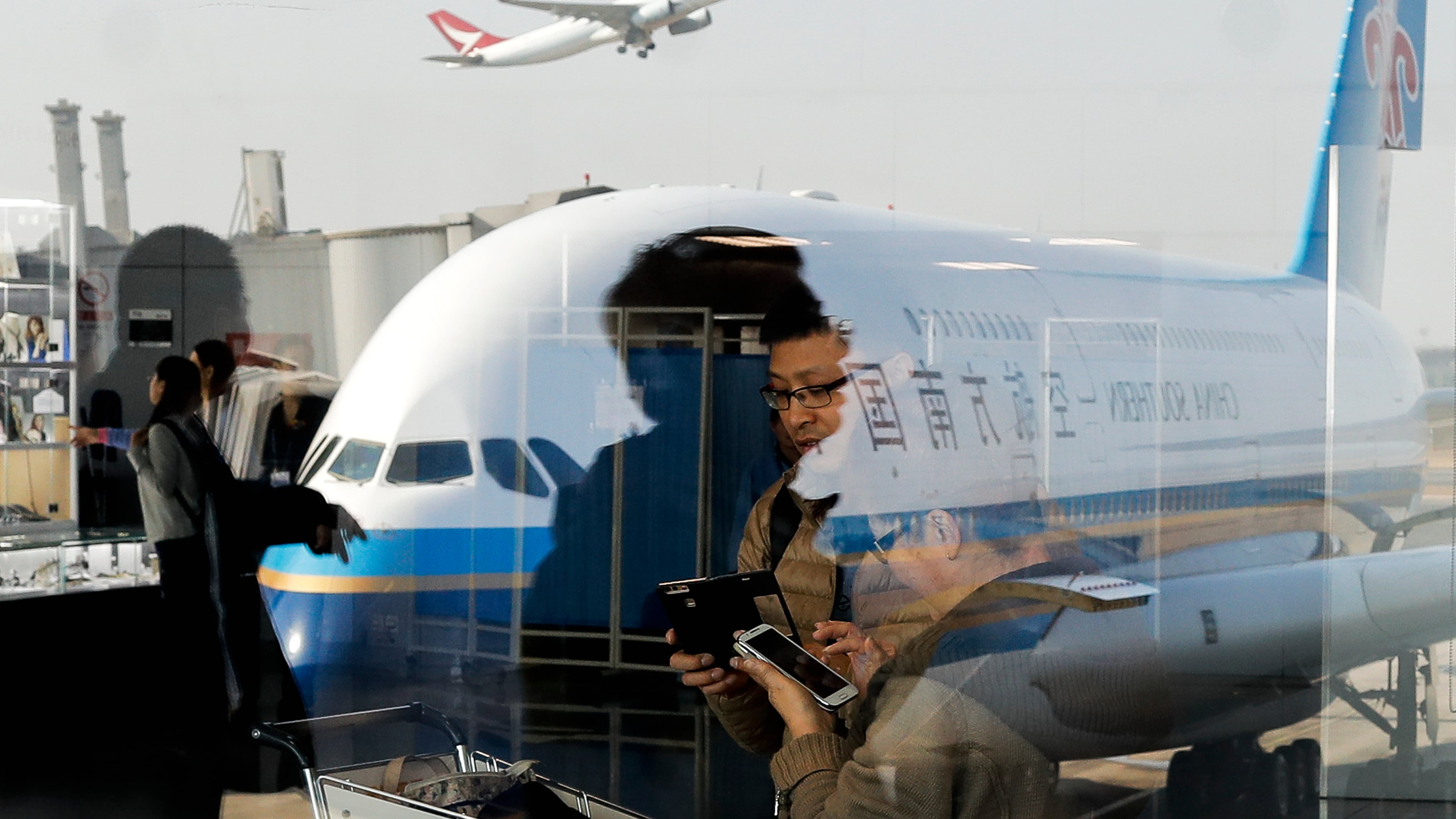 FILE - Passengers walk past a couple browsing their smartphones near a China Southern Airlines, parked on the tarmac at the Beijing Capital International Airport Saturday, Nov. 19, 2016.(AP Photo/Andy Wong, File)