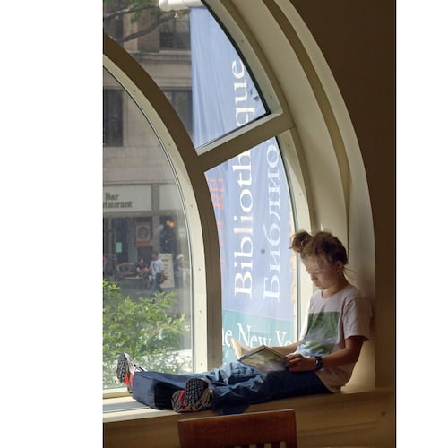 FILE - A young girl reads a book while sitting in a window of the Morningside Heights branch of the New York Public Library on July 29, 2003. (AP Photo/Richard Drew, file)