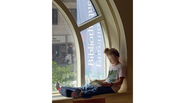 FILE - A young girl reads a book while sitting in a window of the Morningside Heights branch of the New York Public Library on July 29, 2003. (AP Photo/Richard Drew, file)