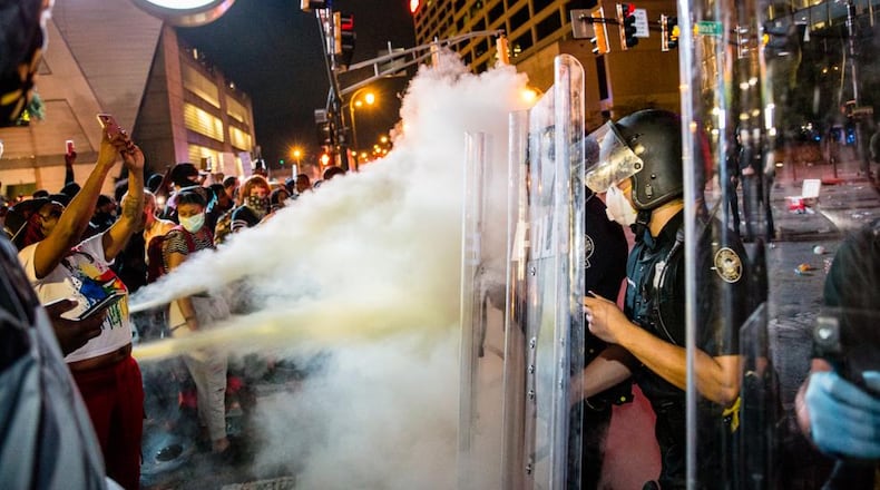 Protesters spray fire extinguishers at police as they clash Friday evening at the corner of Marietta Street and Centennial Olympic Park.