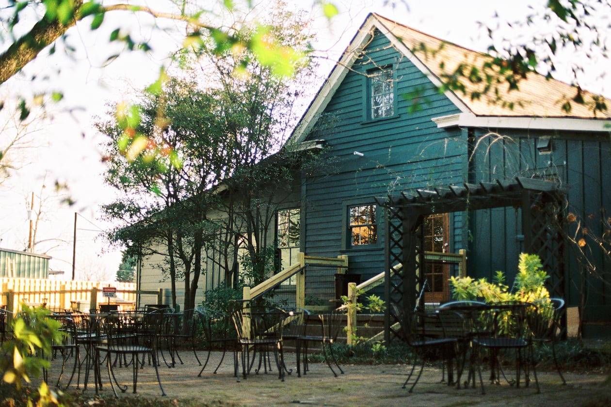 A farmhouse style shop with a patio surrounded by trees