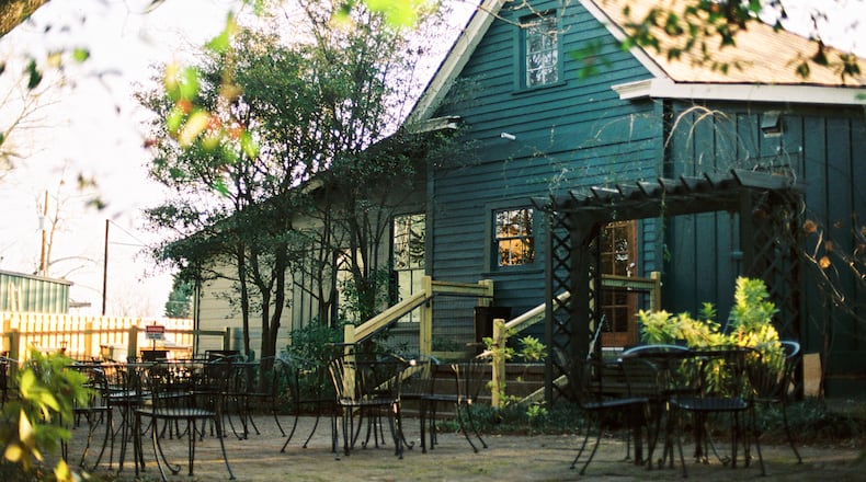 A farmhouse style shop with a patio surrounded by trees