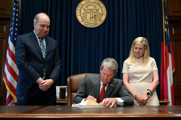 Georgia Gov. Brian Kemp (center) signs the state’s new budget as Rick Dunn (left), director of the Governor’s Office of Planning and Budget, and first lady Marty Kemp stand behind him Tuesday, May 12, 2026, at the Georgia Capitol in Atlanta. (Hyosub Shin/AJC)