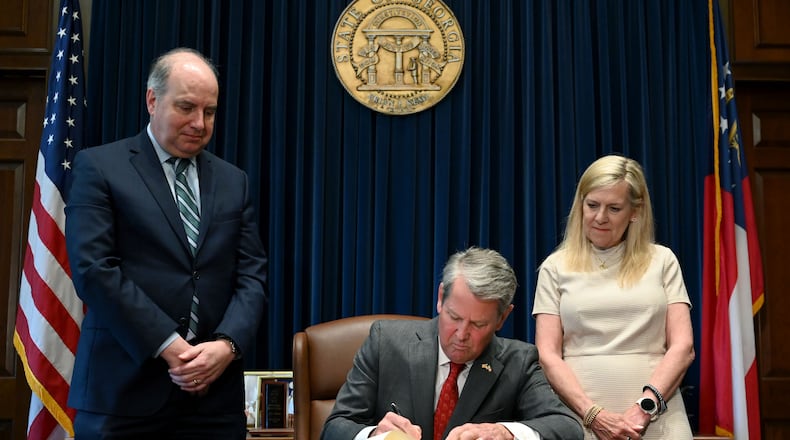 Gov. Brian Kemp (center) signs the state’s new budget alongside Rick Dunn (left), director of the Governor’s Office of Planning and Budget, and first lady Marty Kemp. (Hyosub Shin/AJC)