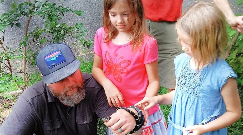 With daughters Ella (center) and Eden looking on, Daniel Ballard, an ecological landscaper, patiently snips plastic mesh netting from an Eastern king snake that had become helplessly entangled in it in a Decatur yard. After being freed, the snake was released into some woods and quickly crawled away. CONTRIBUTED BY CHARLES SEABROOK